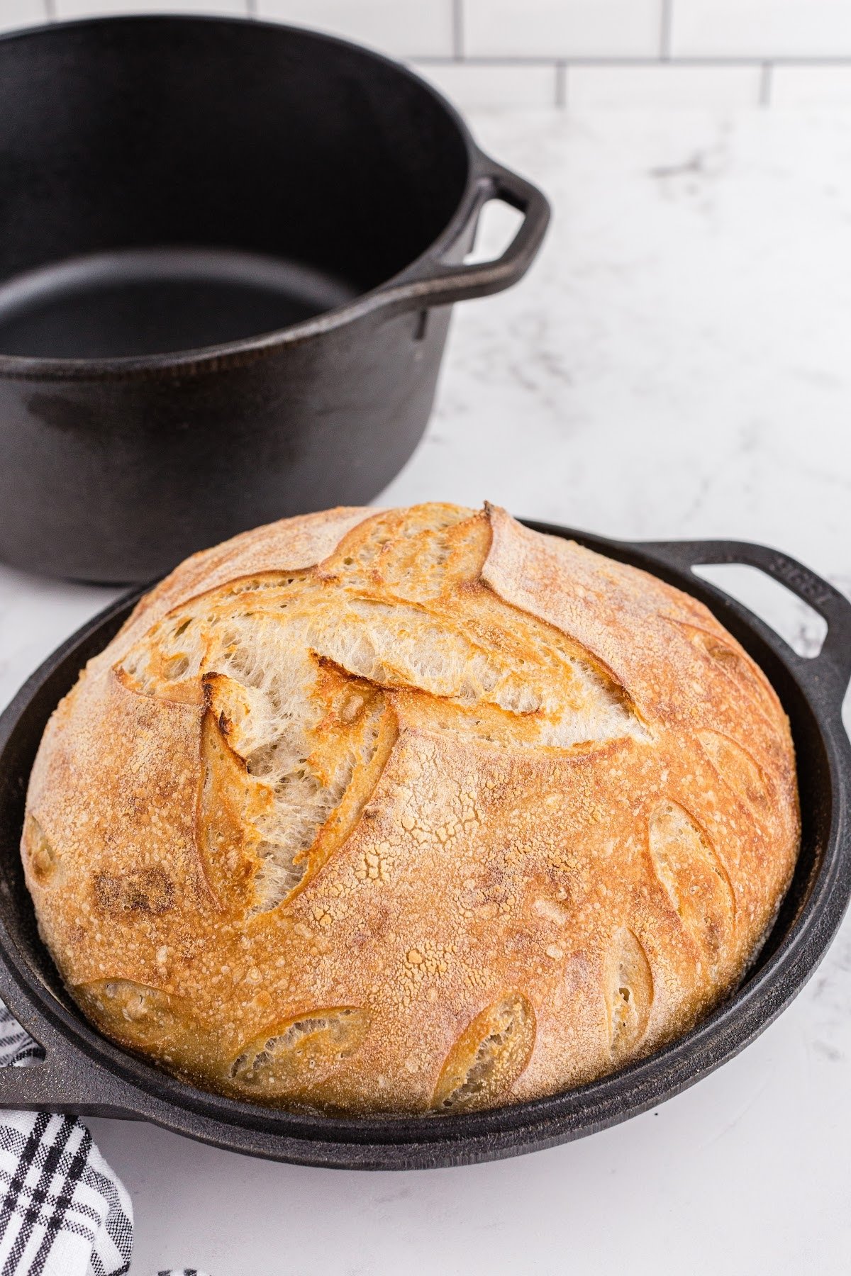 Golden brown baked loaf of basic sourdough bread in cast iron skillet.
