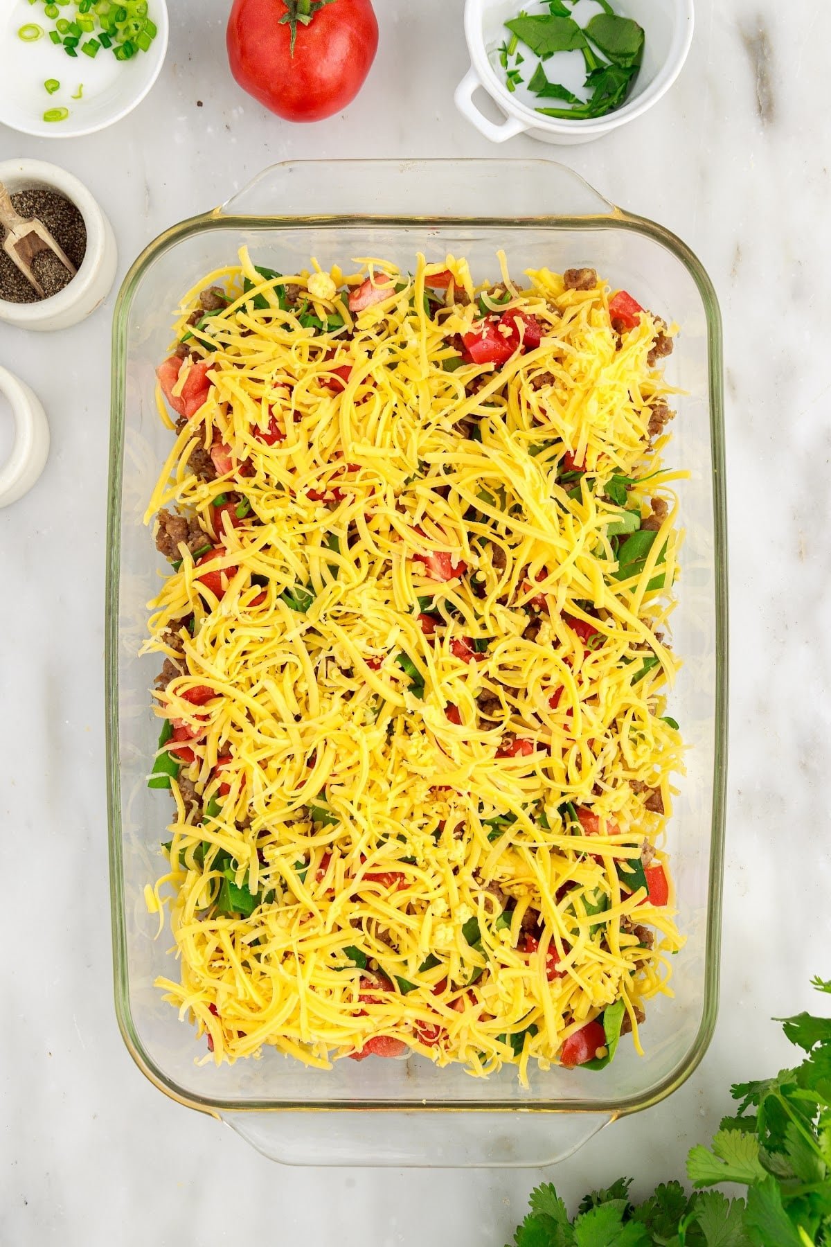 Cheesy egg bake layers in a baking dish with a sprinkle of the remaining shredded cheese on top. ready to be baked.