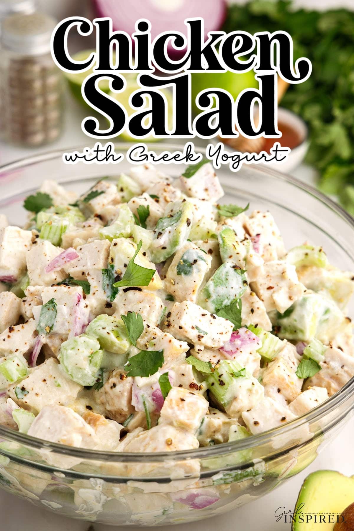 Close up of a glass bowl of chicken salad with Greek yogurt, fresh ingredients in the background.