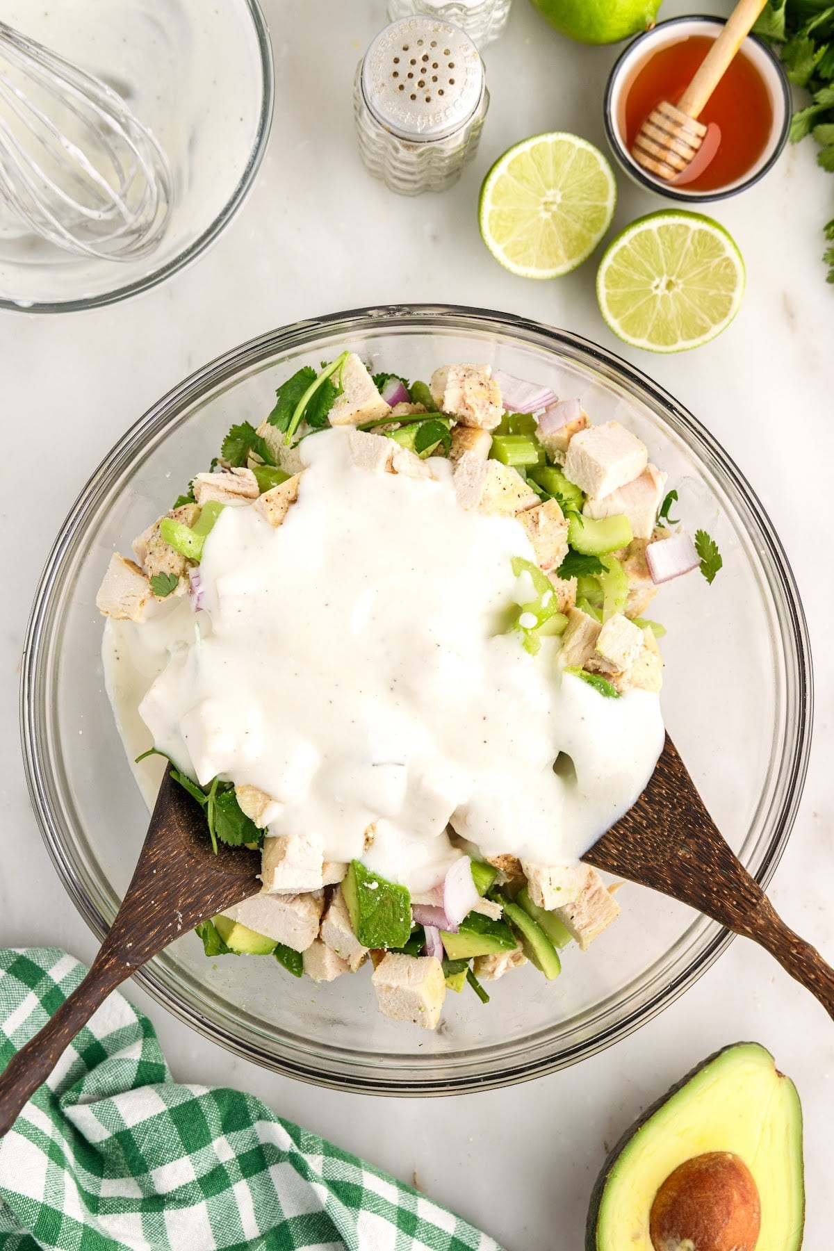 Creamy Greek yogurt salad dressing poured over the freshly tossed chicken salad ingredients in a large glass mixing bowl. 