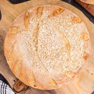 Freshly baked oat sourdough bread on a wooden kitchen board.