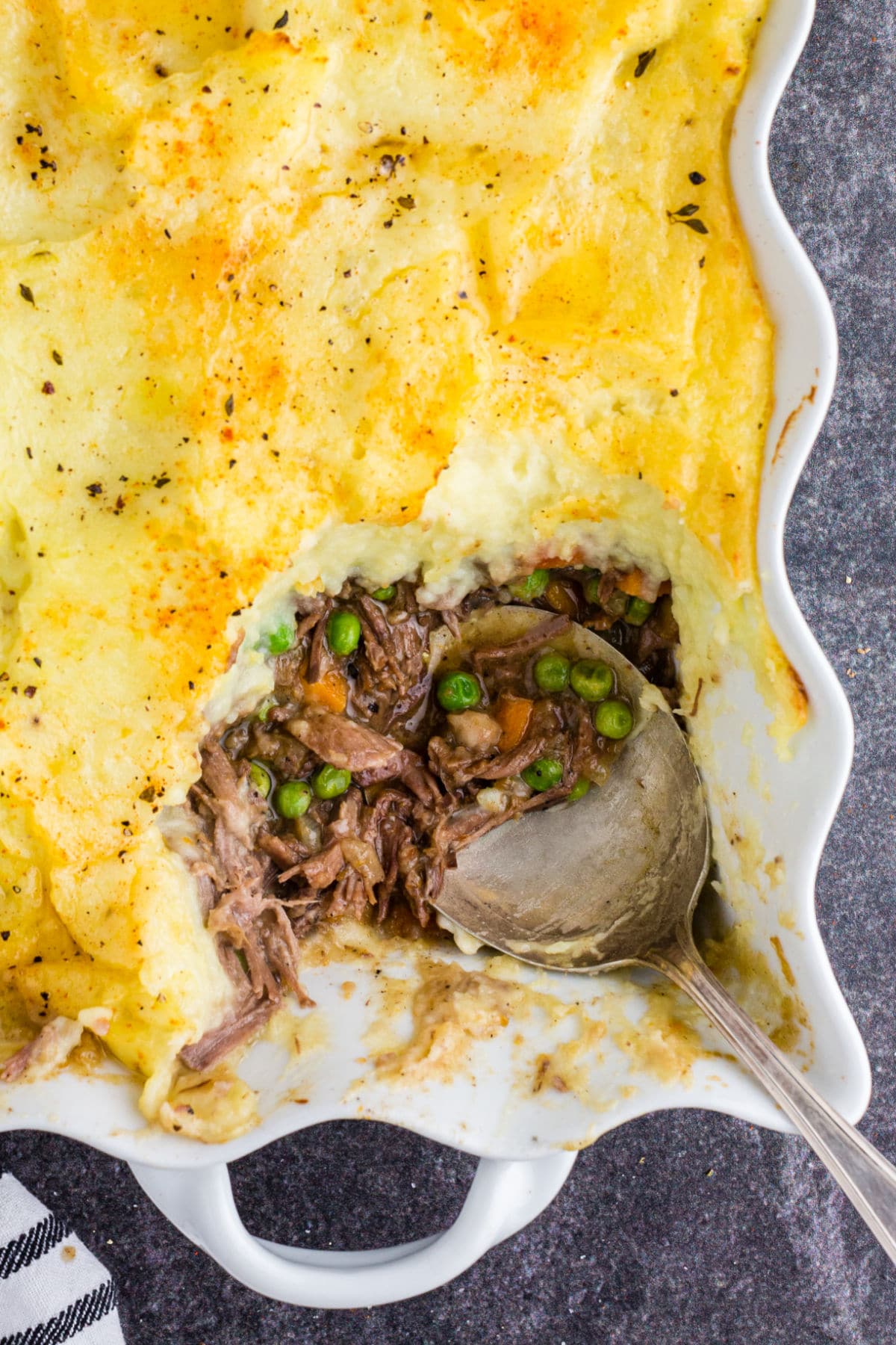 Overhead shot of the baked Shepherd's pie with leftover roast beef, single serving removed with a silver serving spoon resting in the dish.
