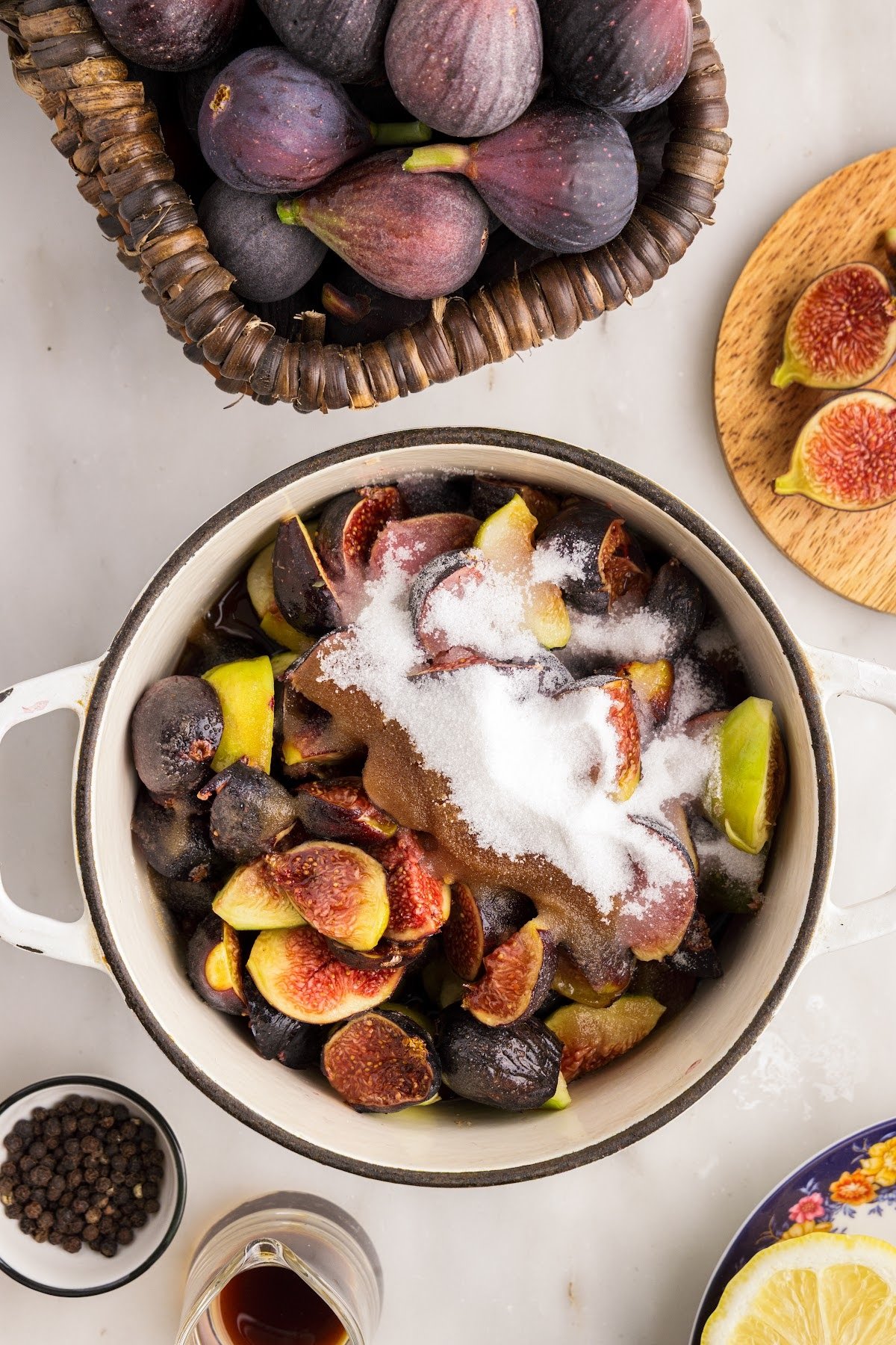 Saucepan with fresh cut figs and sugar, balsamic vinegar, and lemon juice. Fresh ingredients for this jam recipe in the background.