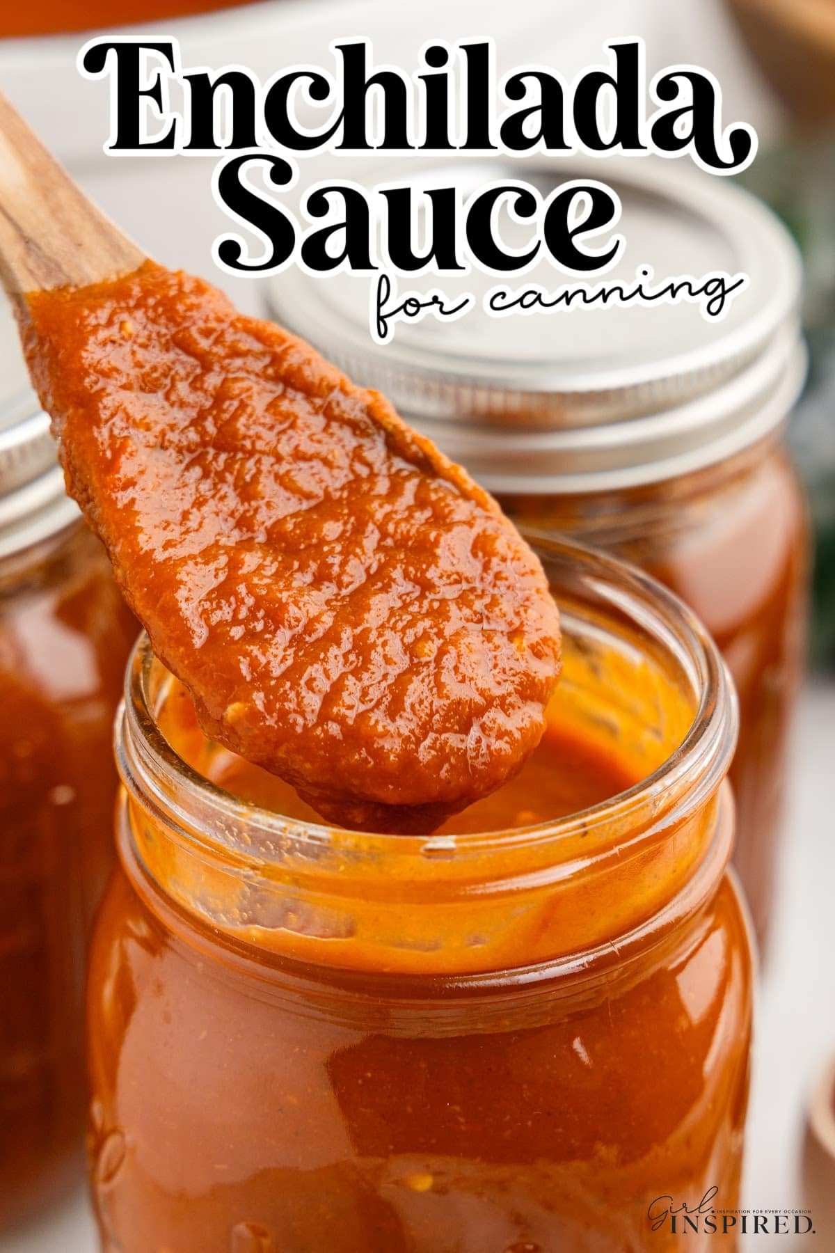 Spoonful of red enchilada sauce over an open jar of red enchilada sauce, more jars of sauce in the background.