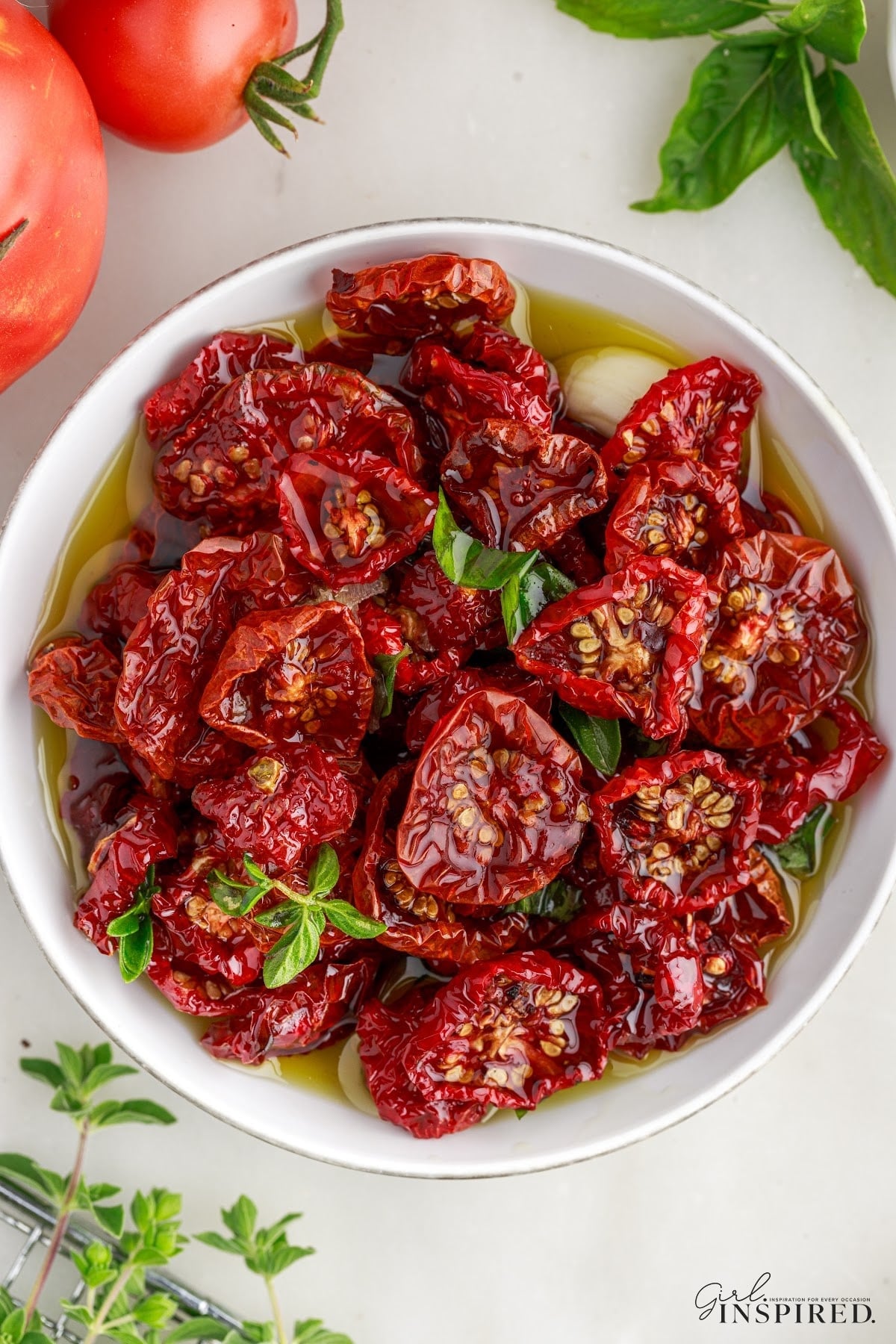Bowl filled with sun-dried tomatoes. Fresh whole tomatoes and fresh herbs in the background.
