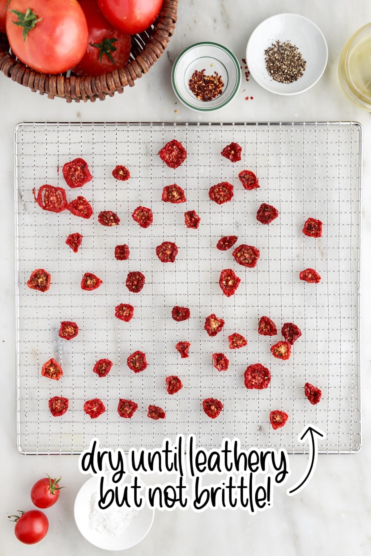 Dehydrated tomatoes on a mesh rack. Fresh tomatoes and spices in the background.
