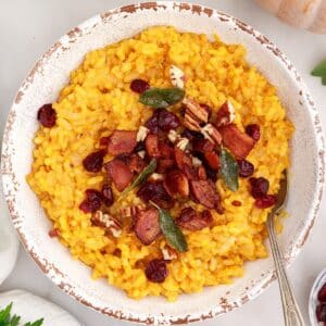 Bowl of baked pumpkin risotto topped with fried sage leaves, crumbled bacon, toasted pecans, and dried cranberries.