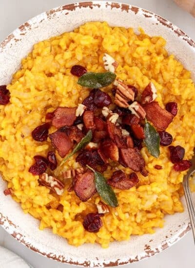 Bowl of baked pumpkin risotto topped with fried sage leaves, crumbled bacon, toasted pecans, and dried cranberries.